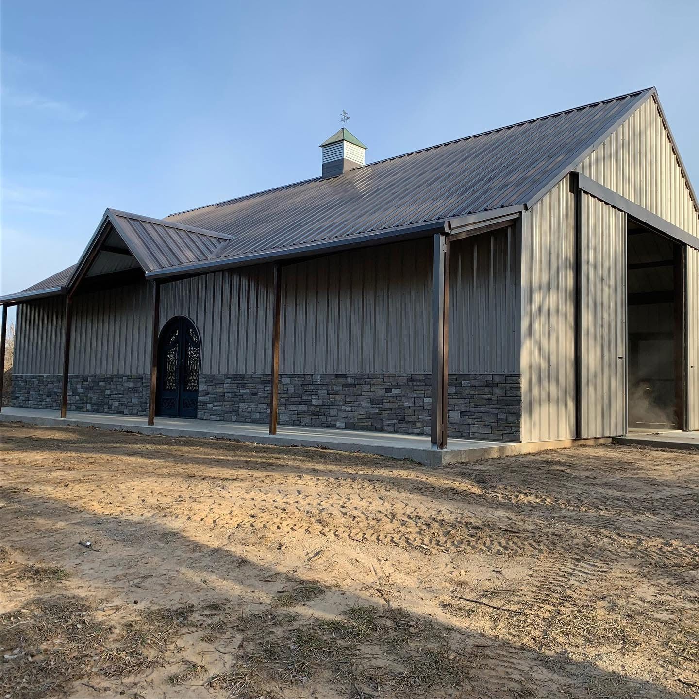 Steel barn with stone wainscot, covered porch and arched iron doors