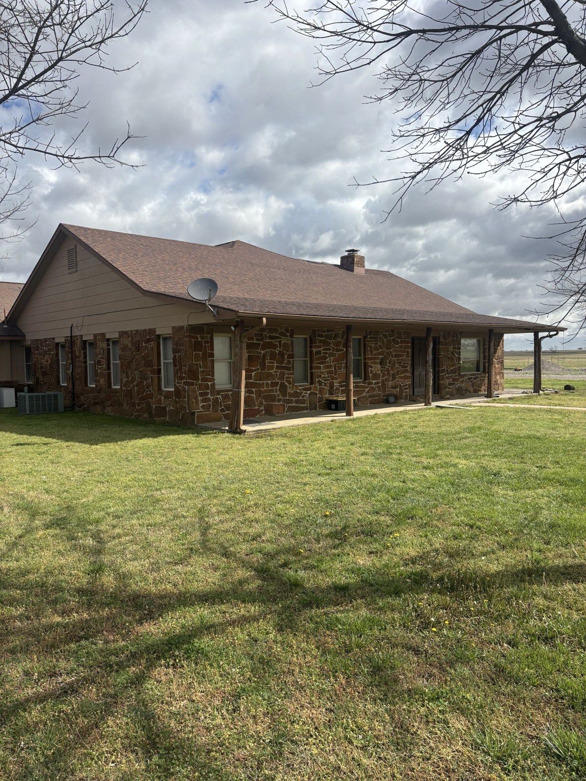 Stone ranch house with tan siding before exterior remodel