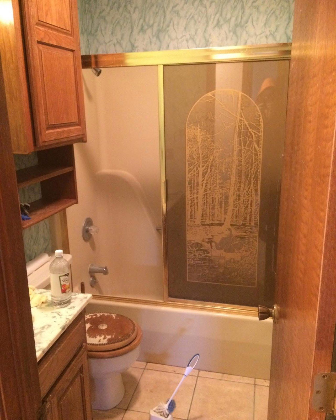 Dated bathroom with etched shower door and wallpaper