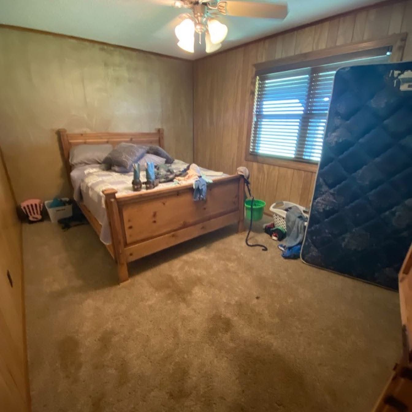 Bedroom before remodel with wood paneling and stained carpet
