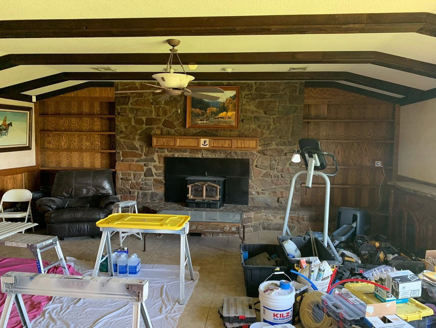 Family room with stone fireplace, dark beams and wood paneling before remodel